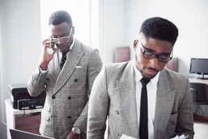 Modern businessman at work. Two confident business people in formalwear discussing something While one of them looks at the documents and the second an important phone call photo
