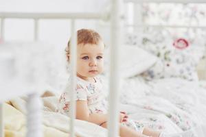 Childhood concept. baby girl in cute dress siting at bed playing with toys by the home. White vintage childroom photo