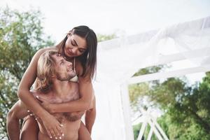 Happy young man wearing his wife on the shoulders of the beach photo