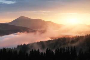 Beautiful sunset in the mountains. Landscape with sun light shining through orange clouds and fog photo