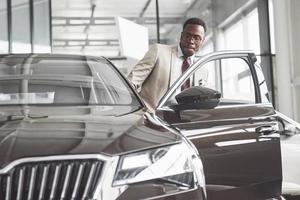 Young black businessman on auto salon background. Car sale and rent concept photo