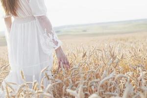 Hermosa chica en vestido blanco corriendo en el campo de trigo de otoño al atardecer foto