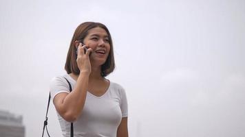 mulher asiática fala com um celular ao lado de um rio.