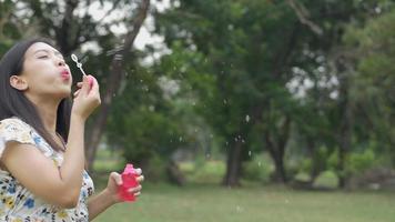 linda mulher asiática jogando bolhas de sabão e se divertindo ao ar livre em um parque público.