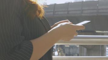 mujer asiática caminando mensajes de texto con un amigo en el teléfono inteligente en la ciudad urbana. video