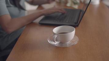 feche uma xícara de café em cima da mesa, tendo uma mulher de fundo trabalhando usando um laptop no escritório. video