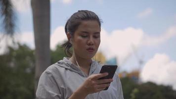corredor de fitness de mulher asiática usando telefone celular, ouvindo música em um parque público. video