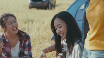 Asian woman happy with friends camping in nature having fun together playing guitar and drinking beer and clinking glasses. video