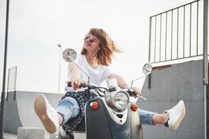 Portrait of a beautiful girl hipster sitting on a black retro scooter, smiling posing and enjoy the warm spring sunshine. photo