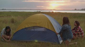 asiatische frauen camping stellen ein zelt auf, während sie bei sonnenuntergang spaß haben, zusammen eine sommerreise. video