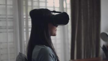 mulher asiática, jogando o jogo e assistindo filme em óculos de vr. garota asiática feliz usando fone de ouvido de realidade virtual 3d em casa. video