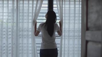 mulher asiática abrindo cortinas na sala em casa. video