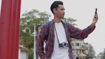 turistas solos de homem asiático em pé usando smartphones com bate-papo por vídeo com amigos no balanço gigante da rua da Tailândia. video