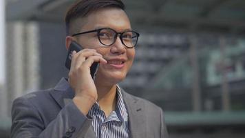 asiatisk affärsman som talar telefon med en vän medan han går på stadsstaden. video
