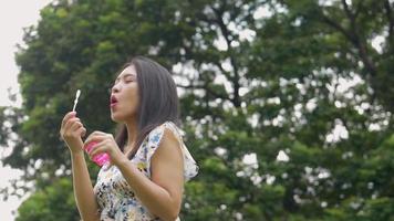 ung asiatisk kvinna som leker såpbubblor och har kul utomhus på en offentlig park. video