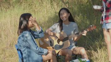 Asian woman happy with friends camping in nature having fun together playing guitar and drinking beer and clinking glasses. video