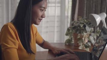 mulher asiática sorrindo feliz curtindo as mãos digitando usando o computador laptop, compartilhando o influenciador do blogueiro de trabalho on-line. video