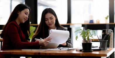 Focused young businesswoman signing agreement with skilled lawyer in eyeglasses. Concentrated financial advisor showing place for signature on paper contract document to male client at meeting