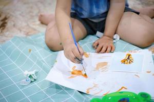 Focus on  hands on paper. Children use paintbrushes to paint watercolors on paper to create their imagination and enhance their learning skills. photo