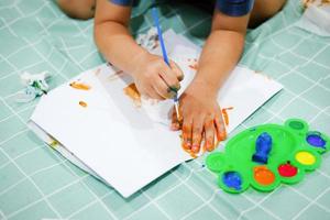 centrarse en sus manos sobre el papel. los niños usan pinceles para dibujar sus manos en el papel para desarrollar su imaginación y mejorar sus habilidades cognitivas. foto
