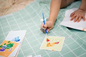 centrarse en las manos sobre el papel. los niños usan pinceles para pintar acuarelas en papel para crear su imaginación y mejorar sus habilidades de aprendizaje. foto