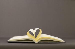 Open book with heart shape on gray background photo