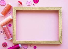 Spools of thread and buttons in pink tones on a pink background photo