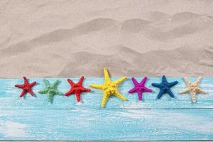 Many starfish of different colors on a wooden board on a sandy beach photo