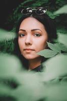 Portrait woman in black clothes and glasses against background of green leaves photo