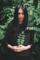 Woman in black dress that holds a twig in her hand against background of forest photo