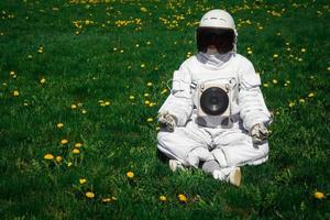 Astronauta futurista en un casco se sienta en un césped verde en una posición meditativa foto