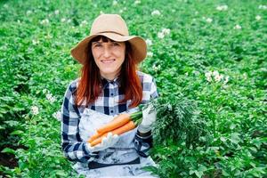 Woman farmer holds a bunch of carrots in her vegetable garden photo