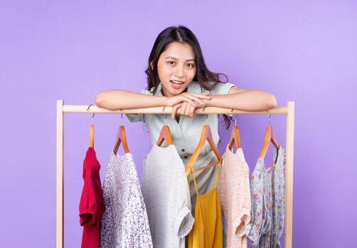 Image of fashion woman in skirt standing near wardrobe with clothes and choosing what to wear isolated on purple background photo