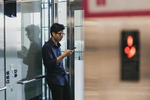 Manos del joven asiático, utilizando un teléfono móvil inteligente, en el ascensor foto