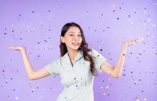 Portrait of a pretty girl standing underneath buying confetti to celebrate, isolated on purple background photo