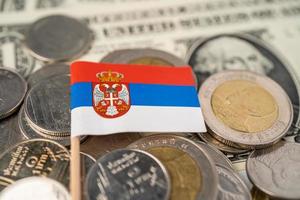 pila de monedas con la bandera de serbia en billetes de dólar estadounidense.