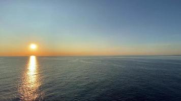 uma visão panorâmica do sol brilhando uma luz dourada no céu da tarde no horizonte, enquanto o vasto mar ondula suavemente enquanto a luz do sol reflete na superfície, seguindo para a esquerda. video