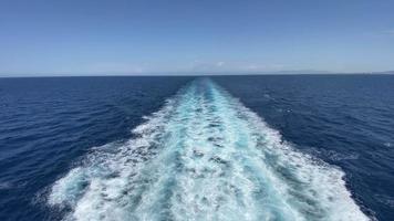 eine erstaunliche Landschaft des weiten blauen Ozeans, die von einem großen Boot aus gesehen wird und an einem sonnigen Tag Wellen und Spritzer auf der Oberfläche erzeugt und rückwärts verfolgt. video