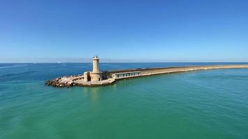 uno splendido scenario di un faro all'estremità di un lungo porto con coste rocciose situato in mezzo al mare vasto e dolce durante il giorno, che si sposta lentamente verso destra. video