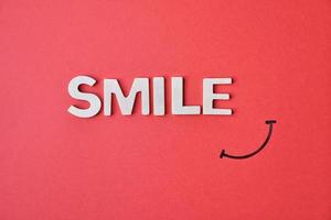 Sonrisa palabra con letras de madera blancas sobre fondo rojo.
