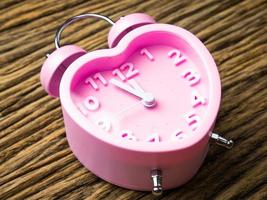 Pink alarm clock in the form of heart on wooden background photo