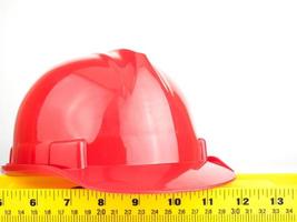 Casco de seguridad rojo y regla de equilibrio sobre fondo blanco, concepto de construcción de ingeniería foto