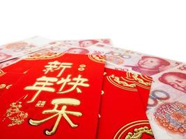 Chinese red envelopes over Chinese money hundred yuan banknotes pile isolated on white background. Chinese text on envelope meaning Happy Chinese New Year photo