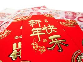 Chinese red envelopes over Chinese money hundred yuan banknotes pile isolated on white background. Chinese text on envelope meaning Happy Chinese New Year photo