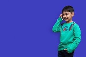 Cute little boy con una camisa verde hablando por teléfono sobre un fondo liso con espacio de copia foto