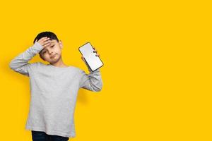 Sonrisa y conmocionado niño chico en camisa gris verde pantalla en blanco del teléfono móvil sobre fondo amarillo espacio de copia