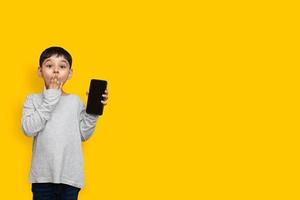 Sonrisa y conmocionado niño chico en camisa gris verde pantalla en blanco del teléfono móvil sobre fondo amarillo espacio de copia foto