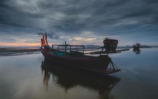 Barco de madera de pesca con luz tenue del cielo al atardecer. foto