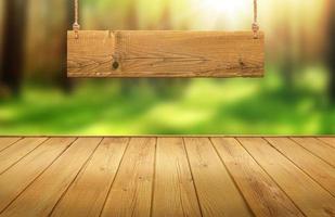 Wood table with hanging wooden sign on green forest blurred background photo