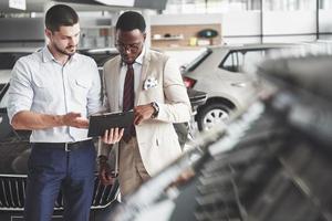 una joven empresaria negra firma documentos y compra un coche nuevo. el concesionario de coches está de pie junto a él foto